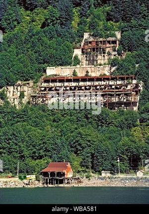 1988 Cette photo montre les ruines de la colline historique de l'usine Alaska Juneau Gold Mining Company qui était en vigueur de 1917 à 1944, à proximité du centre-ville de Juneau, capitale de l'Alaska, USA. La mine a produit 90 millions de tonnes de minerai aurifère, et était l'une des plus grandes mines dans le monde à l'époque. Depuis cette photo a été prise, la forêt d'aulnes ont continué à croître et à cacher ces bâtiments de la mine qui avait été brûlé par des vandales. Dans l'avant-plan est le canal Gastineau qui sert de marine highway à Juneau, une ville à l'eau lié et des navires de croisière destination touristique. Banque D'Images