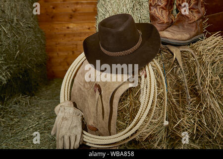 Chapeau de Cowboy de l'ouest avec des gants en cuir, bottes de cow-boy et bottes, et une corde de roper sur le foin dans une grange Banque D'Images