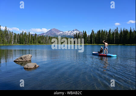 Deux jeunes femmes debout sur paddle board sur Scott Lake, Oregon avec centre et nord volcans en arrière-plan. Soeurs Banque D'Images