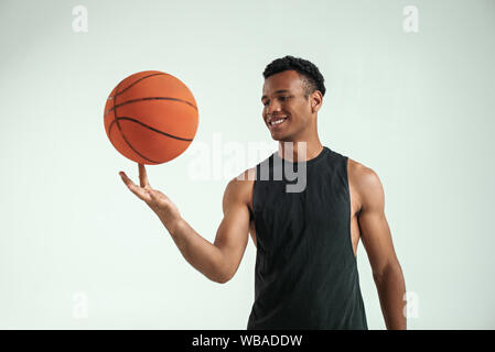 Meilleur joueur. Beau jeune homme africain en vêtements de sport basket ball spinning sur le doigt et souriant tout en se tenant à l'arrière-plan gris. Le basket-ball. Le sport professionnel Banque D'Images