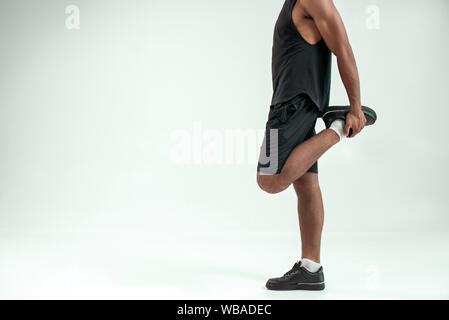 La grande forme. Photo recadrée homme d'étirer la jambe en se tenant contre un arrière-plan gris. Sport concept. Mode de vie actif Banque D'Images