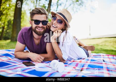 Jeune couple looking at camera and smiling while lying on blanket ensemble dans le parc Banque D'Images