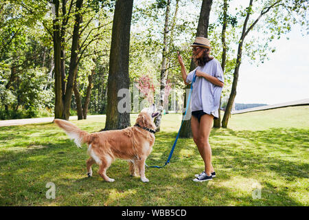 Belle jeune femme avec son chien de formation à l'extérieur et lui donner des gâteries Banque D'Images