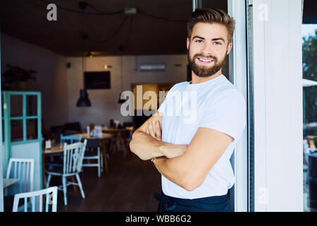 Cheerful young business owner looking at camera with arms crossed while in his restaurant Banque D'Images