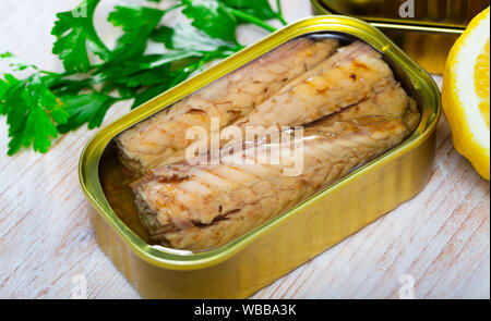 Vue rapprochée de l'ouvert peut de filets de maquereau fumé à l'huile sur table en bois avec citron et verts Banque D'Images