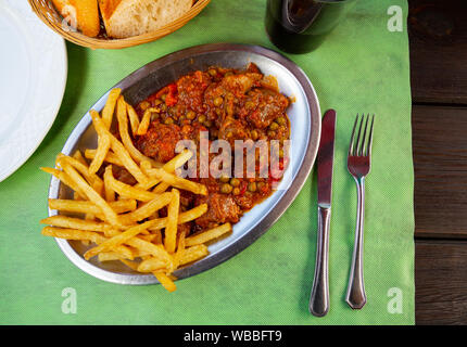 Vue de dessus de l'asturien traditionnel boeuf mijotée dans une sauce aux légumes avec des pois verts servi avec pommes de terre sautées sur plaque de métal Banque D'Images