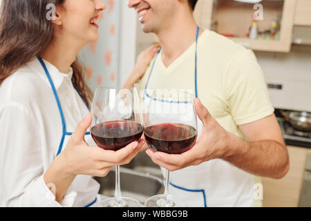 Les jeunes positive woman toasting avec verres de vin lorsque debout dans les tabliers de cuisine en Banque D'Images