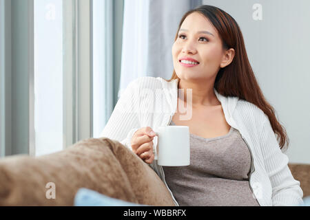Portrait of smiling pregnant Young Asian woman enjoying grand mug de délicieuses boissons chaudes Banque D'Images