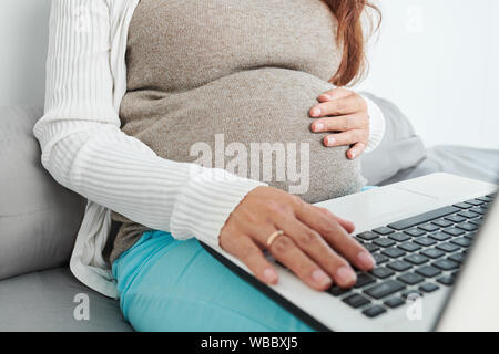 Close-up image of pregnant woman touching her baby coups de ventre et la recherche d'informations sur l'ordinateur portable Banque D'Images