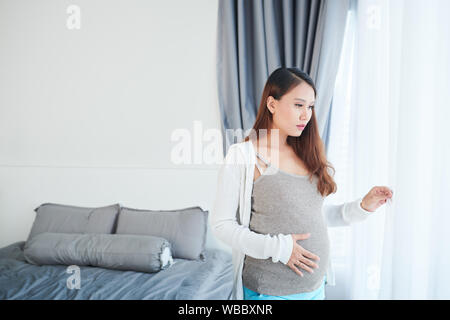 Pensive Young Asian woman opening curtains dans sa chambre à coucher Banque D'Images