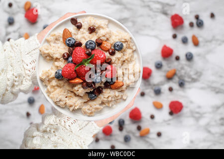 Gruau sain servi avec des petits fruits, de chocolat, amandes et miel. Bol tenue dans une main de femme sur une table de marbre. Tourné à partir de la top vie Banque D'Images