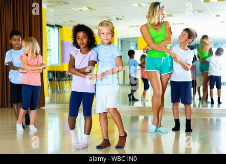 Groupe d'happy smiling enfants pratiquant des mouvements vigoureux jive dans classe de danse avec entraîneur féminin Banque D'Images