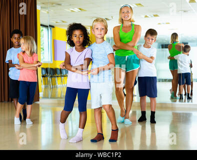 Groupe d'happy happy smiling enfants pratiquant des mouvements vigoureux jive dans classe de danse avec entraîneur féminin Banque D'Images