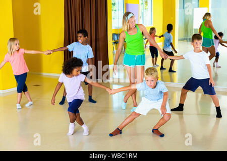 Groupe d'heureux enfants pratiquant des mouvements vigoureux jive dans classe de danse avec entraîneur féminin Banque D'Images