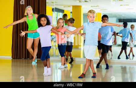 Groupe d'heureux happy smiling enfants pratiquant des mouvements vigoureux jive dans classe de danse avec entraîneur féminin Banque D'Images