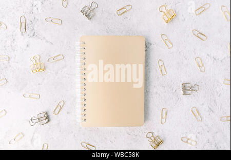 Le bloc-notes de fond sur l'or fermé avec set d'or et d'argent des trombones sur surface de ciment gris clair. Mise à plat. Office de Tourisme et de concept d'entreprise. Banque D'Images