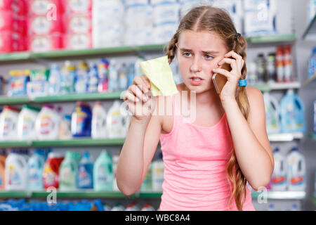 Tween positif fille parlant au téléphone et à la liste de courses au supermarché lors d'une visite Banque D'Images