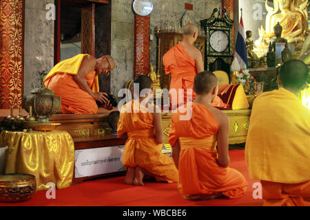 Chiang Mai, Thaïlande - 11.05.2015 - moine bouddhiste plus âgés de prendre photo de jeunes moines novices priant lors de la cérémonie Banque D'Images