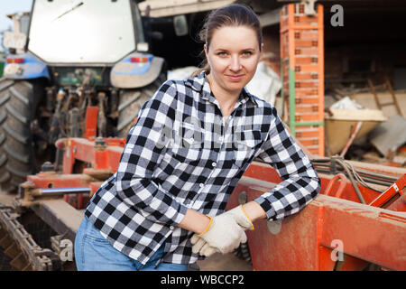 Young woman propriétaire de ferme moderne posant près de tracteur Banque D'Images