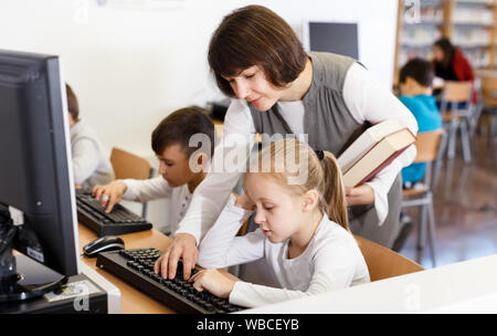 Friendly woman paying tween girl durant la leçon dans la salle informatique de la bibliothèque de l'école Banque D'Images