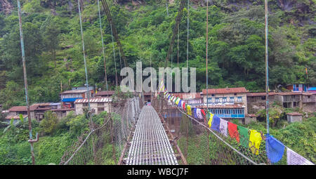 Pont suspendu sur les régions rurales du Népal et les prières d'un drapeau sur le côté Banque D'Images