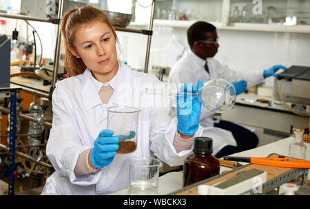 Femme porté des techniciens de laboratoire dans les verres en travaillant avec les réactifs et les tubes à essai, l'homme sur l'arrière-plan Banque D'Images