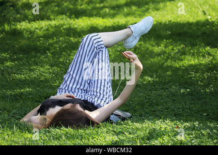 Girl lying on a Green grass avec le smartphone et décisions. selfies Jeune femme se détendre en été, le parc de loisirs de concept sur la nature, regardant la vidéo Banque D'Images