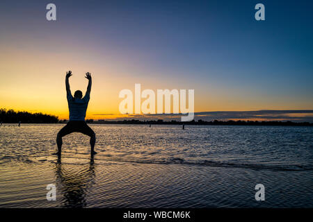 Lever du soleil silhouette d'un homme debout dans l'eau peu profonde et en pratiquant des mouvements de tai chi ou chigong, Boyd Lake State Park dans le nord du Colorado Banque D'Images