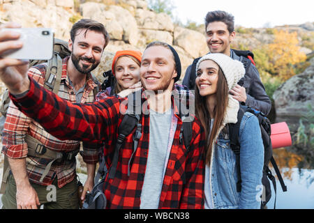 Groupe de jeunes professionnels amis transportant des sacs à dos sur une randonnée ensemble, en tenant un selfies Banque D'Images
