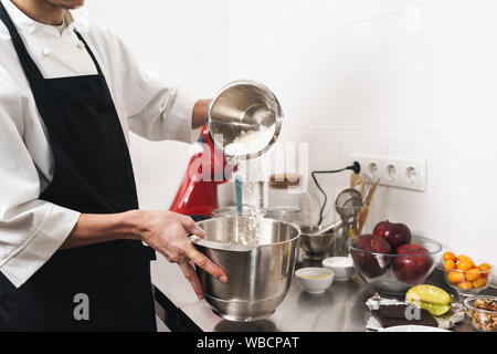 Photo recadrée d'un beau jeune cuisinier chef à la cuisine la cuisson à l'intérieur. Banque D'Images