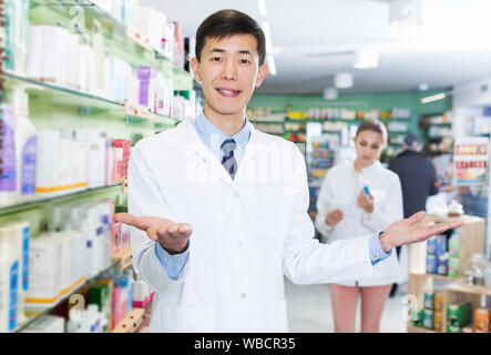 Portrait of smiling japanese male spécialiste qui est debout près de selves en pharmacie. Banque D'Images