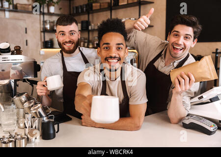Groupe d'hommes gais baristas portant des tabliers travaillant au comptoir de café à l'intérieur Banque D'Images