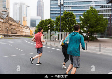 Photo de l'arrière de l'athletic jeunes gens portant des vêtements d'entraînement et faire running on city street Banque D'Images