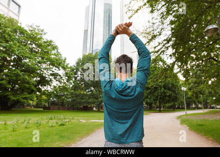 Photo de l'arrière de l'athletic man wearing sportswear faisant d'entraînement et s'étend son bras à city park Banque D'Images
