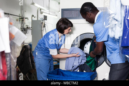 Les travailleurs qualifiés de blanchisserie avec son collègue masculin africain loading lave-linge avec les vêtements sales Banque D'Images