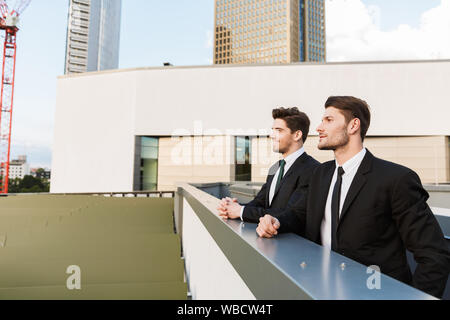 Deux jeunes hommes d'affaires attrayant confiant convient de porter à l'extérieur à l'article les rues de la ville, discuter d'un nouveau projet Banque D'Images
