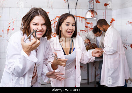 Deux jeunes filles s'amusant avec des amis masculins en quête prix en chambre chirurgicale avec des traces de sang, qui posent avec des instruments médicaux Banque D'Images