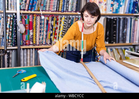 Vendeuse compétente a ordonné de mesure pour la coupe de tissu textile en boutique, la préparation pour la vente Banque D'Images