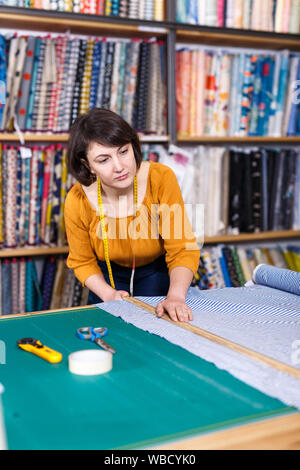 Vendeuse compétente a ordonné de mesure pour la coupe de tissu textile en boutique, la préparation pour la vente Banque D'Images