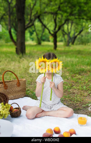 Girl holding sunflower devant faire face à l'extérieur. Fête en plein air dans le jardin, pique-nique. Banque D'Images