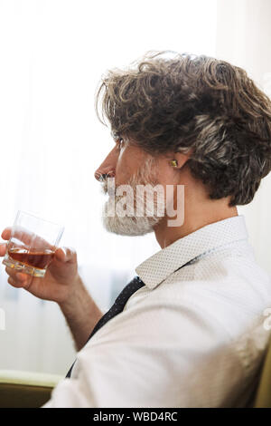 Vue latérale photo d'un beau brun gris senior business man sitting in chair à l'intérieur à la maison l'alcool. Banque D'Images