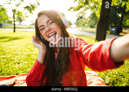 Image de Funny Girl avec étudiants langue à l'aide de casques et de prendre des photos tout en restant assis dans selfies green park Banque D'Images