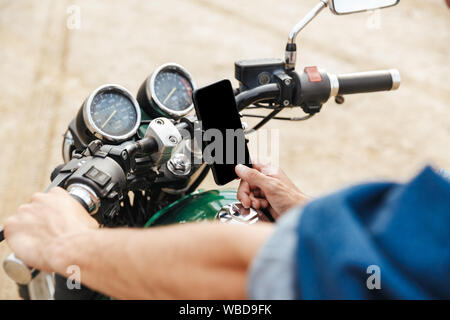 Close up of a man holding guidon et à l'aide de téléphone mobile tout en étant assis sur une moto à la plage Banque D'Images