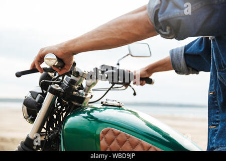 Close up of a man holding guidon tout en étant assis sur une moto à la plage Banque D'Images