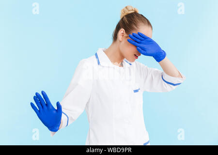 Belle blonde femme médecin en uniforme isolés sur fond bleu, couvre le visage avec la main Banque D'Images