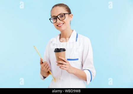 Beautiful smiling blonde femme médecin en uniforme isolés sur fond bleu, tandis que le bloc-notes de café à emporter d'alcool Banque D'Images