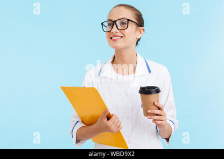 Beautiful smiling blonde femme médecin en uniforme isolés sur fond bleu, tandis que le bloc-notes de café à emporter d'alcool Banque D'Images