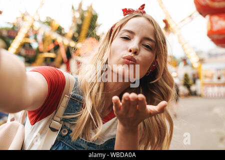 Image de jolie blonde femme portant des vêtements fille soufflant de l'air et baiser photo selfies à amusement park Banque D'Images