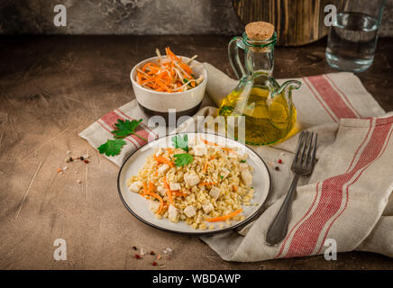 Pilaf de boulgour au poulet dans une assiette et un bol de salade de chou sur un béton fond brun Banque D'Images