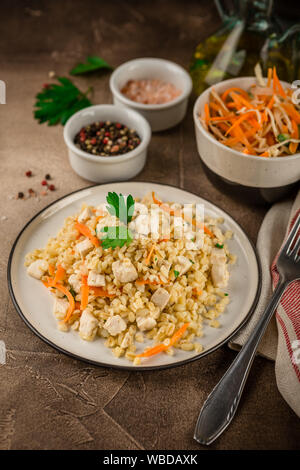 Pilaf de boulgour au poulet dans une assiette et un bol de salade de chou sur un béton fond brun Banque D'Images